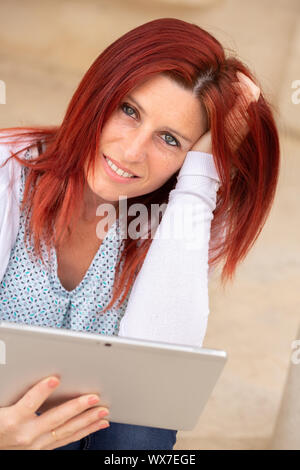 Ritratto di un bel rosso-donna dai capelli con un sereno il viso e le mani nei capelli mediante una compressa Foto Stock