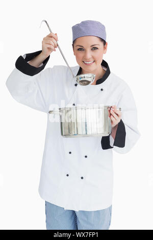 Felice cook che serve con un mestolo e una pentola nella parte anteriore della fotocamera Foto Stock