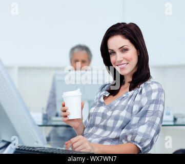 Imprenditrice radiante tenendo un bicchiere alla sua scrivania in ufficio Foto Stock