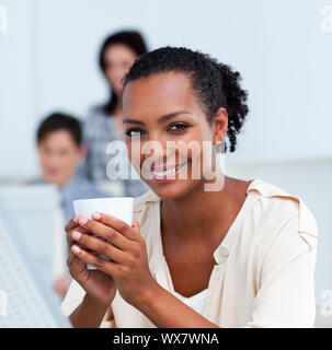 Incandescente imprenditrice di bere un caffè alla sua scrivania in ufficio Foto Stock