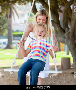 Jolly madre spingendo la figlia su un altalena in un parco Foto Stock