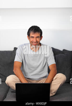 Uomo felice usando un computer portatile su un divano grigio Foto Stock