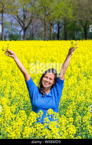 Felice giovane donna le braccia in alto in giallo campo di colza Foto Stock