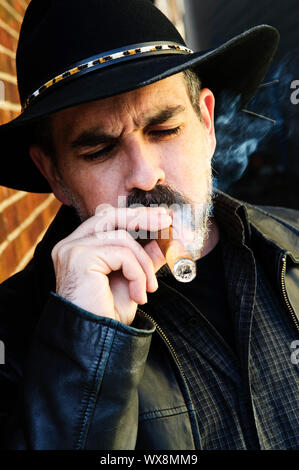 Uomo con la barba nel cappello da cowboy di fumare il sigaro Foto Stock