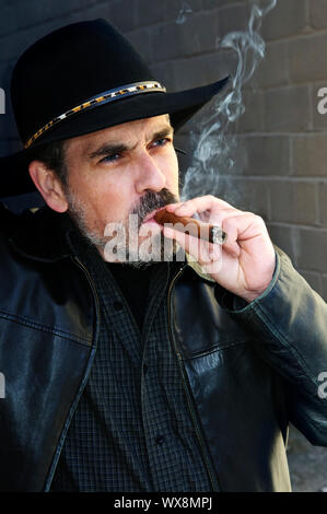 Uomo con la barba nel cappello da cowboy di fumare il sigaro Foto Stock