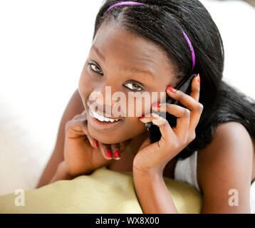 Incandescente afro-adolescente americano parlando al telefono di sorridere alla telecamera giacente su un divano contro uno sfondo bianco Foto Stock