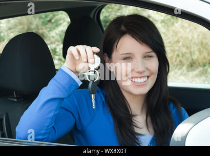 Adolescente radiante tenendo premuto i tasti auto seduto nella sua nuova vettura sorridente verso la telecamera Foto Stock