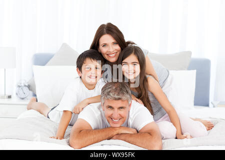 Happy familly guardando la telecamera sul loro letto Foto Stock