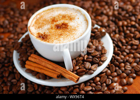 Tazza di cappuccino con cannella e versato fuori i chicchi di caffè. Foto Stock