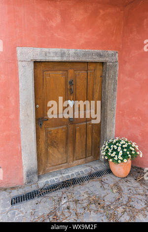 Bassa e piccola cantina porta con una a forma di cuore e di ornamento vaso di fiori in una vecchia casa davanti Foto Stock
