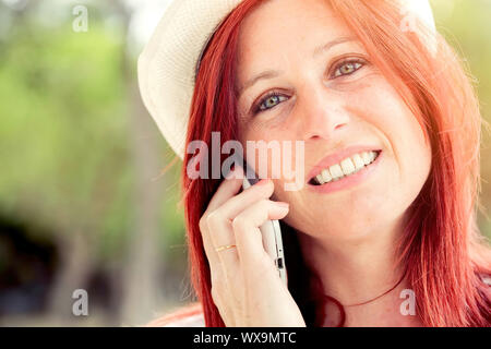 Ritratto di sorridente bella giovane donna close up con telefono cellulare, sullo sfondo di estate green park. Foto Stock
