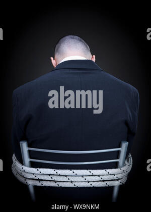 Un imprenditore è legato su una sedia girando le spalle alla telecamera. Foto Stock