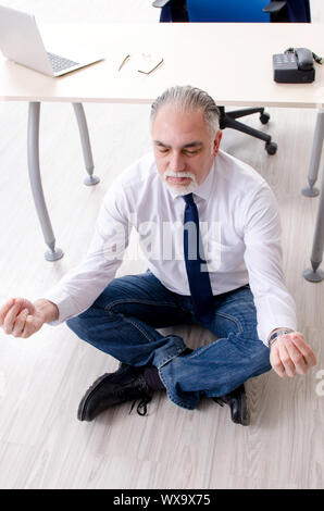 Imprenditore invecchiato facendo esercizi yoga in ufficio Foto Stock