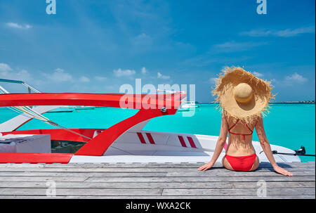 Donna in bikini seduta sul molo con la barca Foto Stock