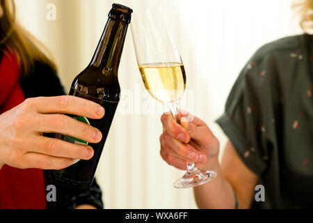 Due donne che fanno un brindisi con una bottiglia di birra e un bicchiere di champagne Foto Stock