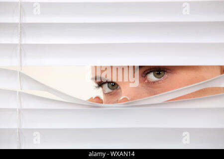 Donna del peering attraverso persiane Foto Stock