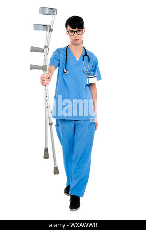 Triste medico tenendo su stampelle in mano e camminare verso la telecamera. Foto Stock
