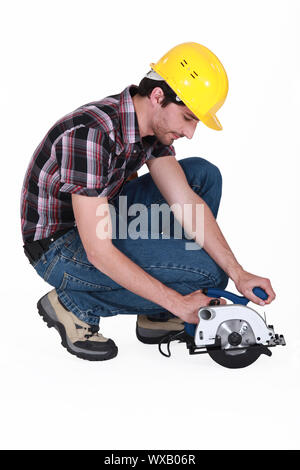 Uomo in ginocchio per utilizzare una sega circolare Foto Stock