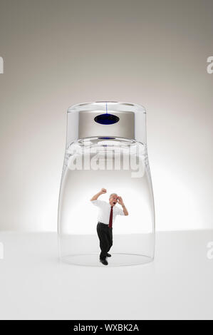 Studio concettuale di immagine di un diminutivo grey-haired senior business uomo intrappolato sotto un elegante e moderno in vetro o bicchiere martellare i pugni contro il Foto Stock