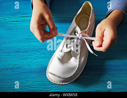 Il ragazzo è imparare come legare lacci delle scarpe, close-up sulle mani e Bianco Pelle Scarpa su legno color turchese Foto Stock