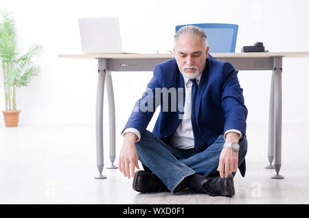 Imprenditore invecchiato facendo esercizi yoga in ufficio Foto Stock