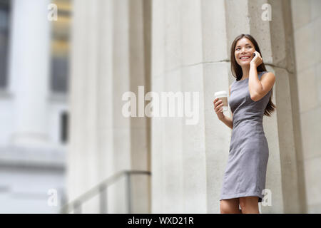 Avvocato imprenditrice professional passeggiate all'aperto a parlare sul cellulare smart phone di bere il caffè dalla carta monouso cup. Multirazziale Asian / Caucasia Foto Stock