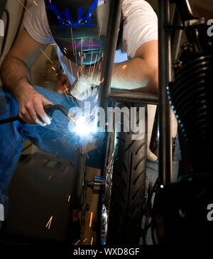 Saldatrice a lavorare sulla forcella metallica di un motociclo Foto Stock