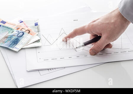 Vista ritagliata di un uomo rivolto alla relazione finanziaria con denaro euro su un tavolo. Foto Stock