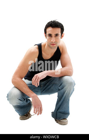 Bello grave Caucasian ragazzo indossa serbatoio nero top e jeans squatting, isolato Foto Stock