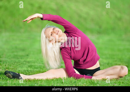 Bella giovane donna facendo esercizio di stiramento su erba verde al parco. Lo Yoga Foto Stock