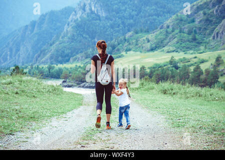 Madre e figlia sono tra le montagne su una strada di campagna con la mano Foto Stock