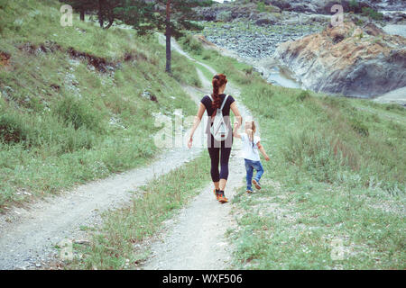 Madre e figlia sono tra le montagne su una strada di campagna con la mano Foto Stock