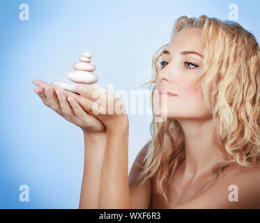 Ritratto di donna carina holding spa pietre in mano isolato su sfondo blu, godendo dayspa, meditazione yoga, equilibrio zen Foto Stock