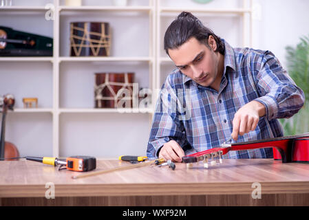 Giovane bello repairman riparazione di chitarra Foto Stock