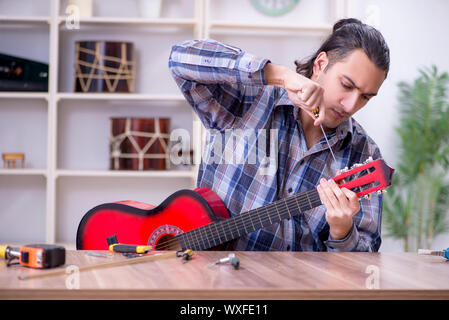 Giovane bello repairman riparazione di chitarra Foto Stock
