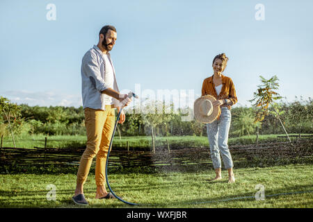 Giovane uomo e donna di irrigazione prato verde, avendo cura del bel cortile in campagna Foto Stock