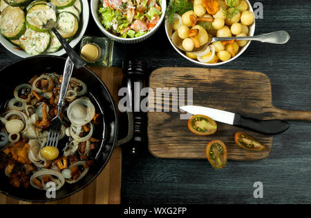 Verdure sullo sfondo. Zucchine fritte salsa in una piastra. Giovani patate bollite con aneto in una ciotola. Fried chanterelle poltiglia Foto Stock