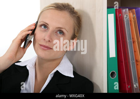 Imprenditrice appoggiata contro la libreria durante una chiamata Foto Stock