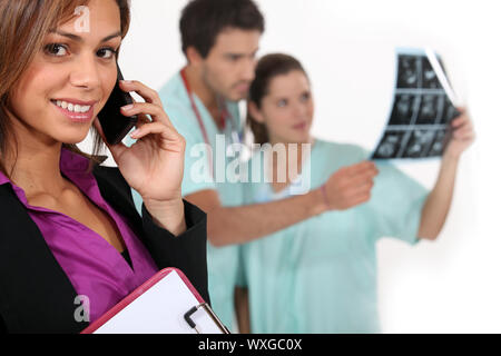 Ospedale manager su un telefono come i medici guardare a raggi x in background Foto Stock