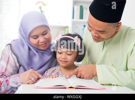 Malay musulmana di insegnamento dei genitori Bambino la lettura di un libro. Sud-est asiatico la famiglia a casa. Foto Stock