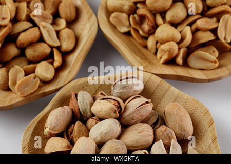 Piastre in legno di arachidi salate e pistacchi su sfondo bianco. snack alla birra Foto Stock