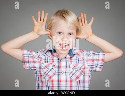 Un simpatico cheeky giovane ragazzo sorridente e attaccando le dita negli orecchi e tirando una divertente volto. Isolato su bianco. Foto Stock