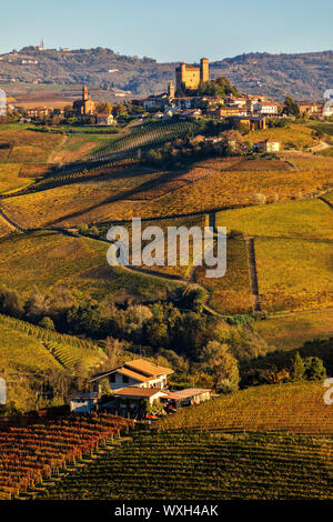 Vista di variopinti vigneti autunnali e il piccolo borgo medievale sulle colline delle Langhe in Piemonte, Italia settentrionale. Foto Stock