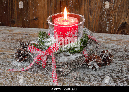 Naturale natale decorazione: un ardente candela rossa in una lanterna circondato da una corona di ramoscelli su un asse di legno. Foto Stock