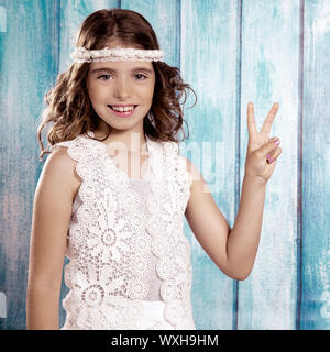 Brunette happy hippie Bambini ragazza sorridente con la pace segno a mano in legno di colore blu Foto Stock