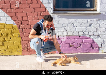 Animali domestici e animali concetto - bel giovane uomo gioca con il simpatico gatto rosso all'aperto Foto Stock