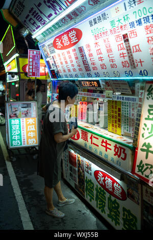 Taichung, Taiwan: piccola cucina di strada fornitore con una enorme scelta di vendere un varietà di latte e bevande base frutta in un mercato notturno. Le donne acquistare bevande Foto Stock