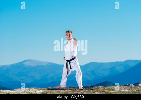 Bionda atleta di karate non kata sulla cima di una montagna mentre si esegue una linea di calci, pugni e blocchi sulla cima di una montagna in una giornata di sole. Foto Stock