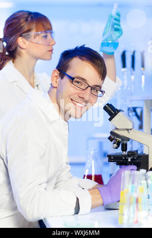 Ritratto di un giovane ricercatore maschio microscopia in scienze della vita (forensics, microbiologia, Biochimica, Genetica, oncologia...)laboratorio. Femmina Foto Stock