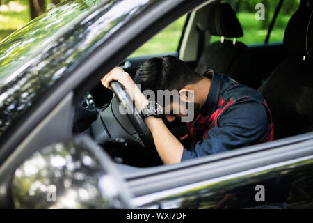 Closeup ritratto stanco giovane uomo bello con breve durata dell'attenzione, alla guida della sua auto dopo lunghe ore di viaggio, cercando di rimanere sveglio a ruota, unità organizzativa isolato Foto Stock